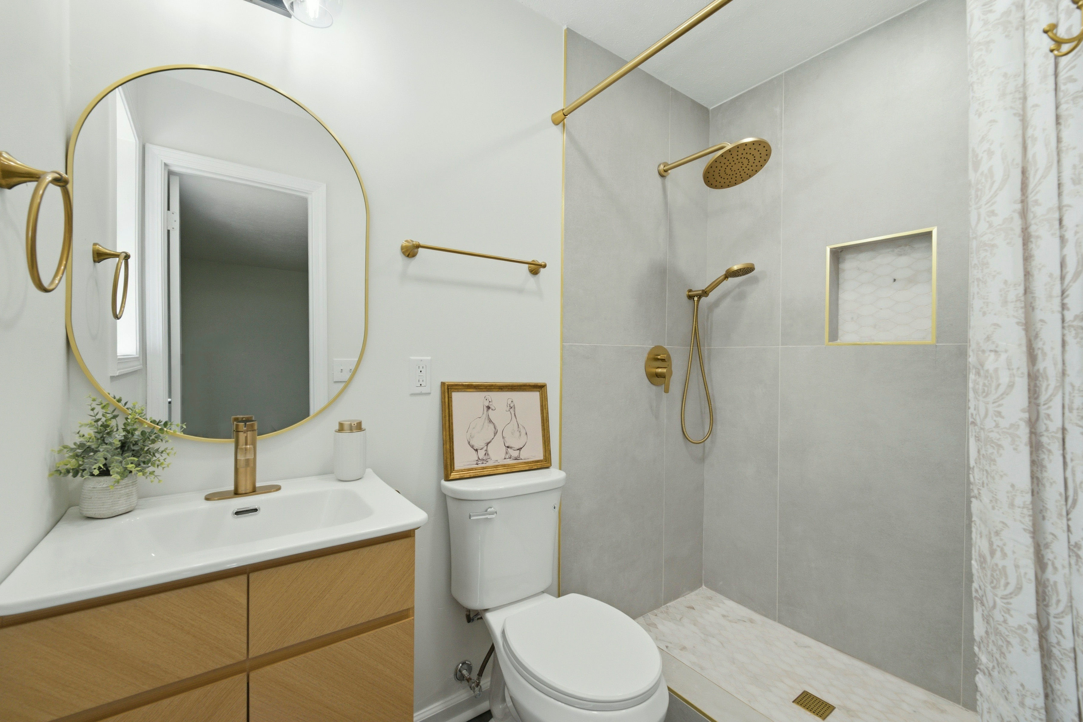 Bathroom with gold fixtures, round mirror, and gray tile shower