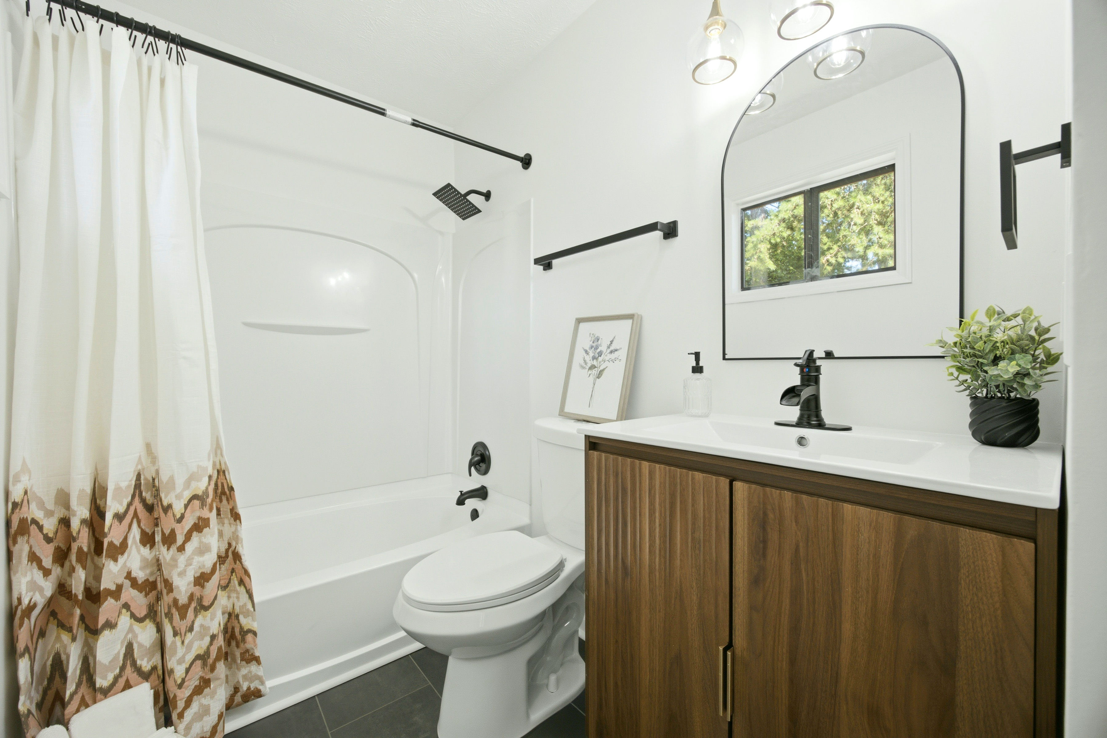 Bathroom with walnut vanity, black fixtures, and tub