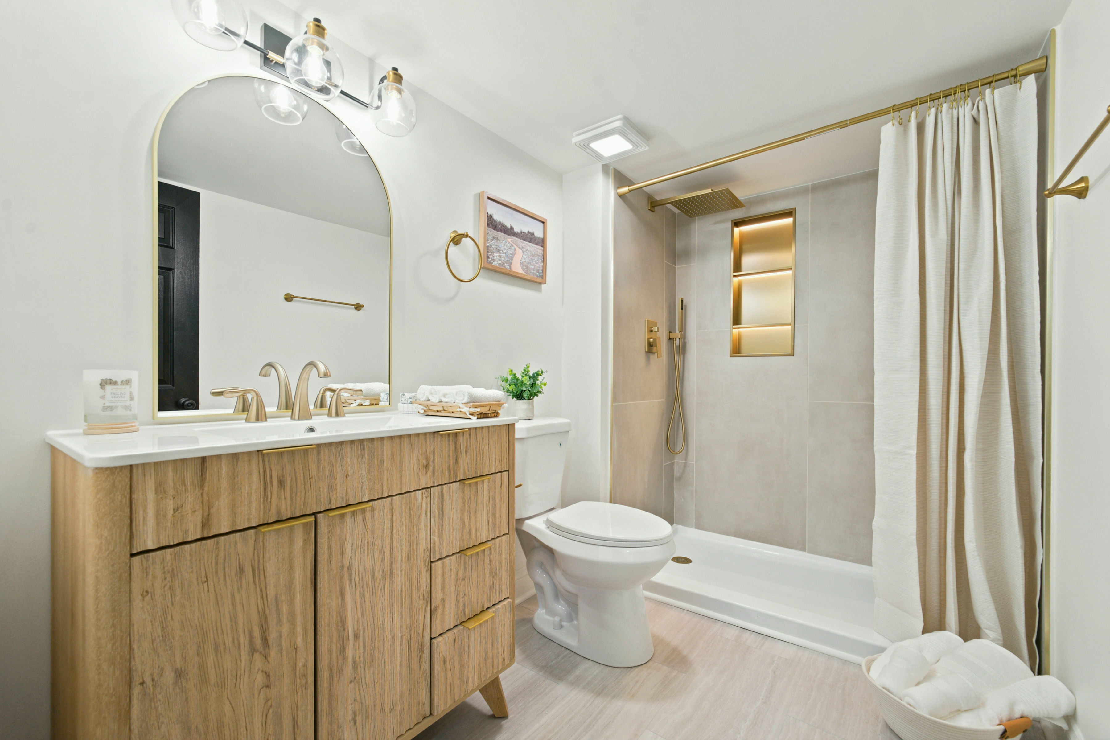 Bathroom with wood vanity, gold fixtures, and tile shower