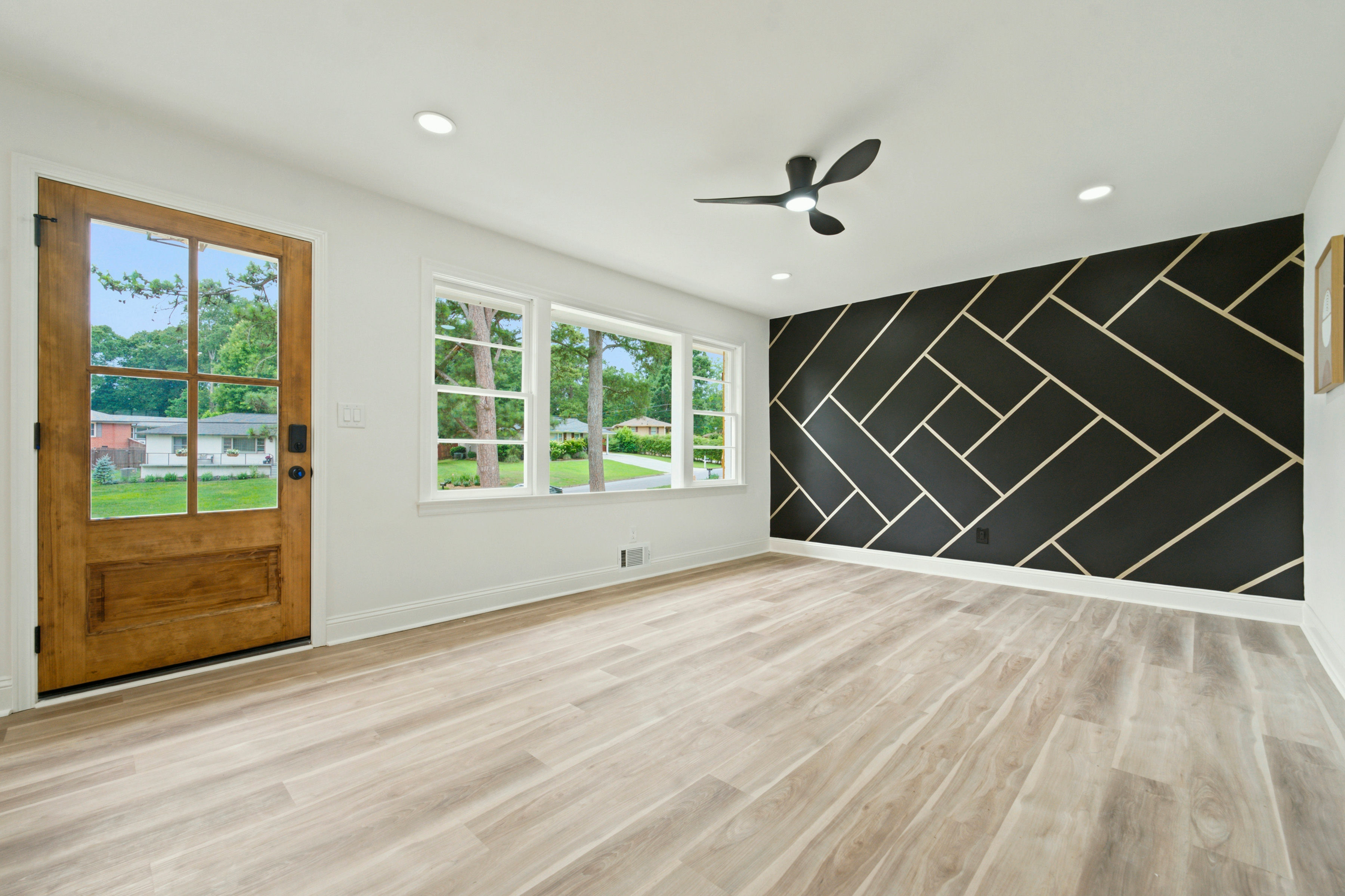 Entry with wood door, light floors, and black geometric accent wall