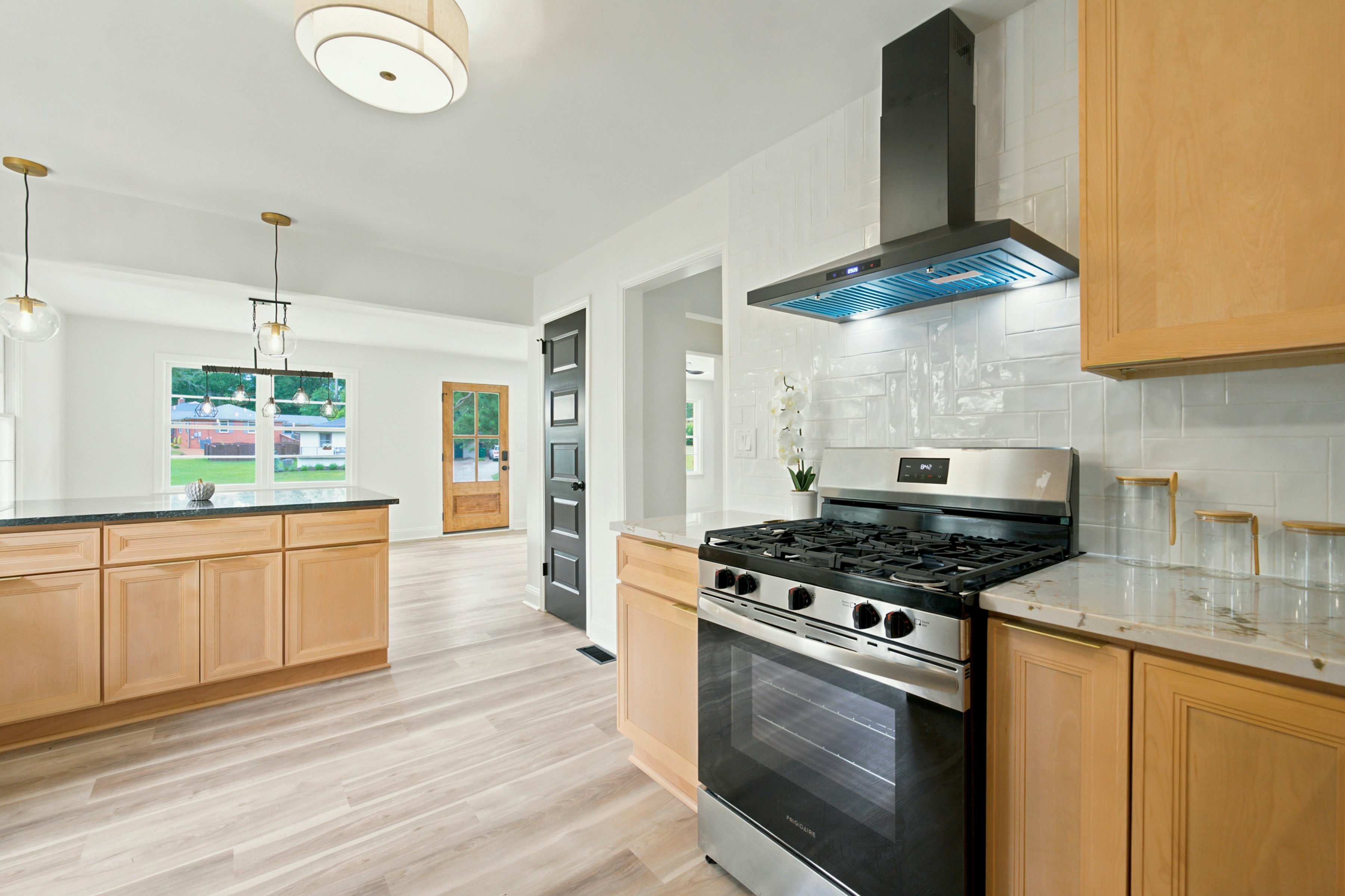 Light wood kitchen with gas range and herringbone tile backsplash