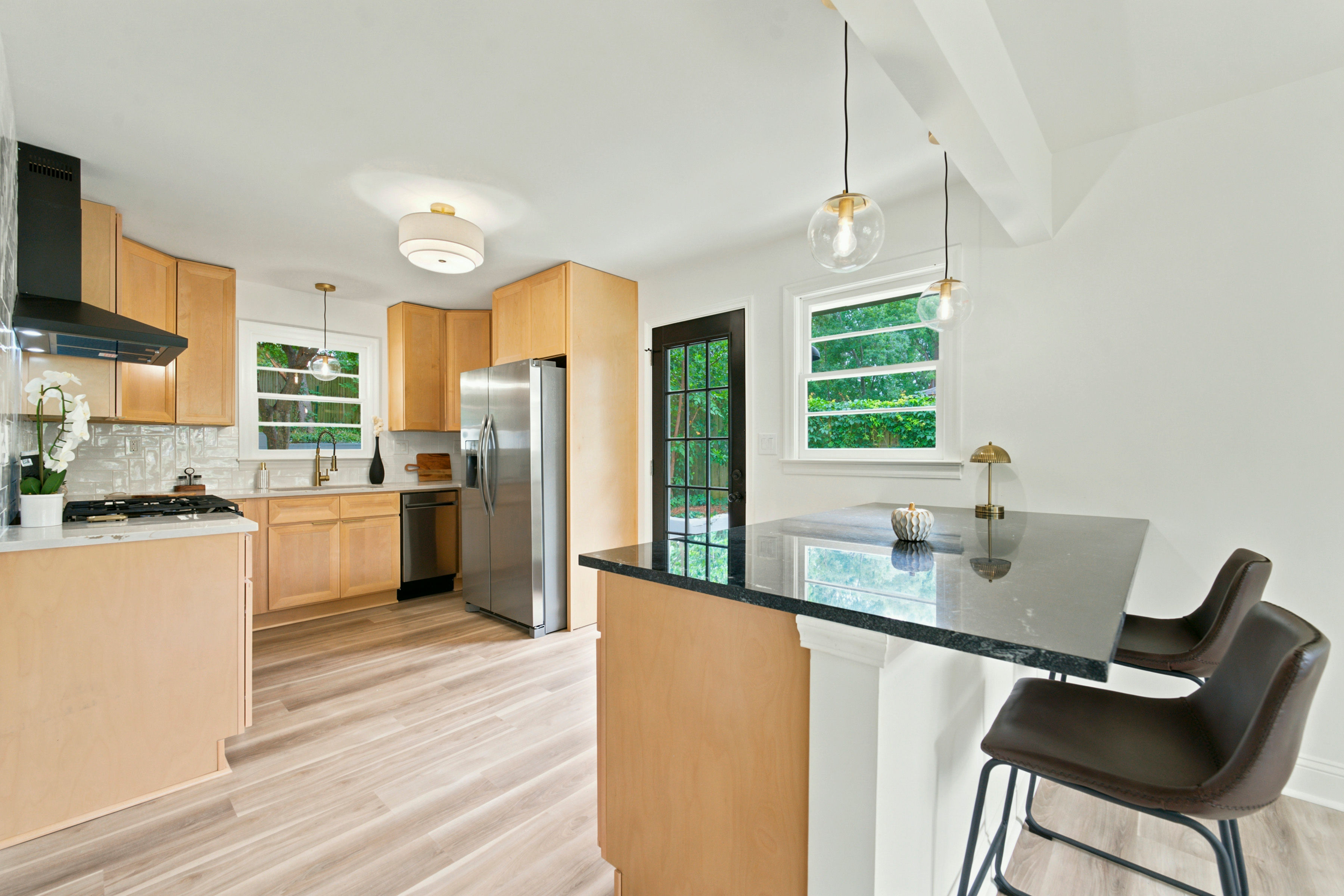 Light wood kitchen with black stone island and bar stools