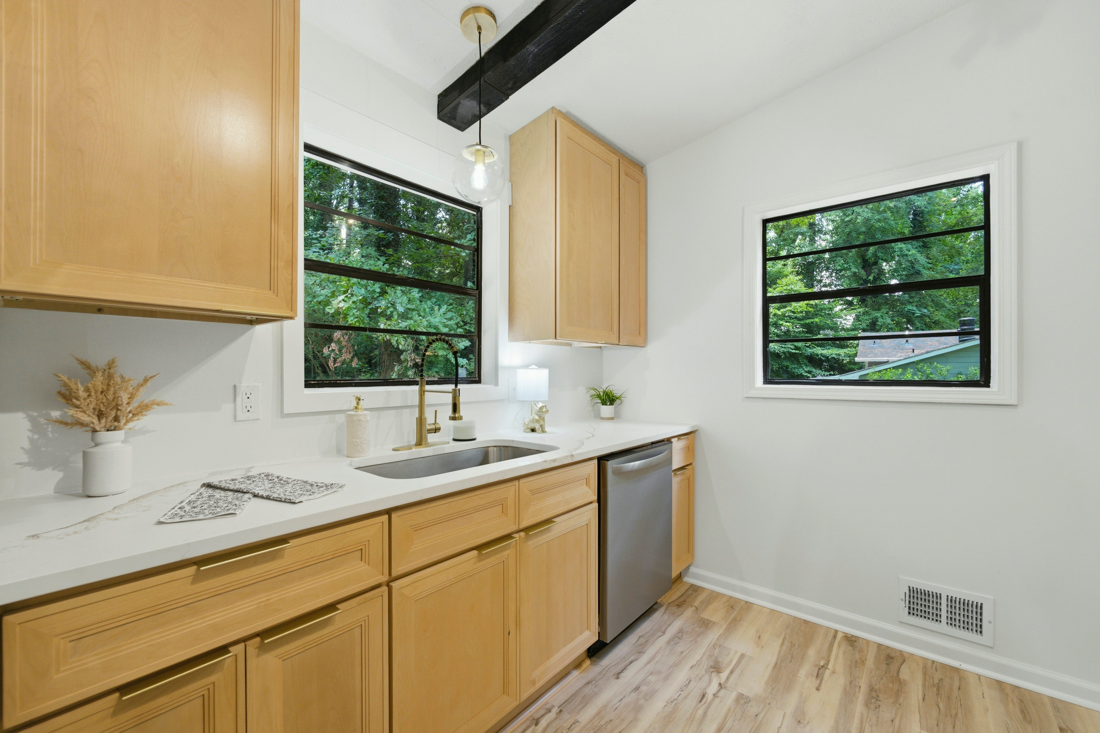 Light wood kitchen sink with gold faucet and black-frame windows